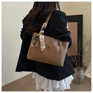 Borsa tote marrone con dettaglio sciarpa di seta indossata da modella in interno chic