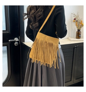 Detailed view of ginger suede crossbody bag with long tassels on a female model
