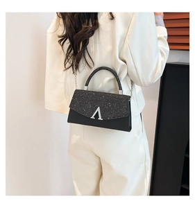 Détail d'un sac carré noir avec chaîne argentée et rabat pailleté sur un costume blanc cassé