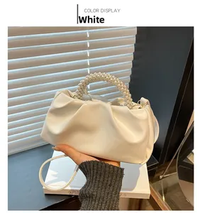 Detail of white ruched crossbody bag with a delicate pearl bead handle on a wooden table