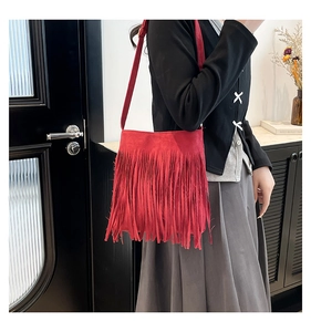 Detail view of red fringed faux suede crossbody bag worn by model in casual home setting
