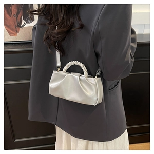 Detail of pleated shoulder bag with a beaded pearl handle and adjustable strap worn by model