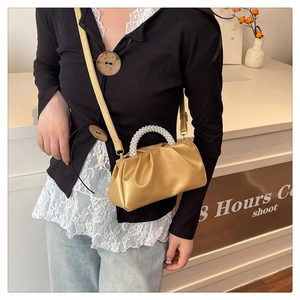Detail of golden brown pleated bag with pearl handle and slim crossbody strap