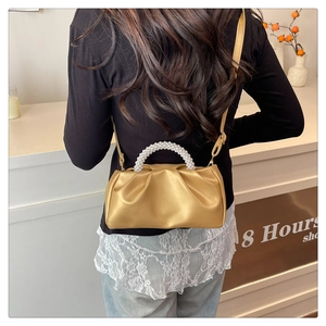 Golden pleated cloud bag with pearl handle shown crossbody on a model in a boutique
