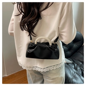 Detail of black pleated cloud bag featuring pearl handle and slim crossbody strap