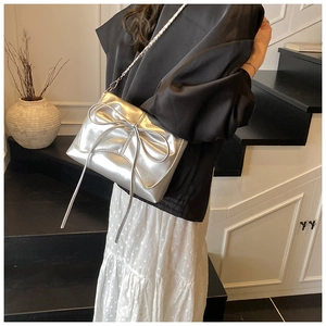 Detail van metallic zilveren schoudertas met grote strik en kettingriem op model