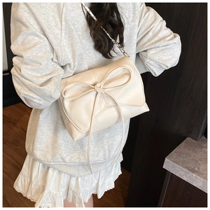 Close-up of a cream shoulder bag featuring a large bow and metallic woven chain strap