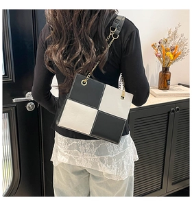 Detail of black and white checkerboard square bag with gold chain strap on model