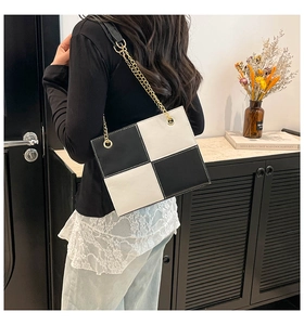 Detail view of stylish black and white checkered crossbody bag with gold chain strap