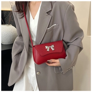 Detail of red crossbody bag with crocodile texture flap and silver bow decoration