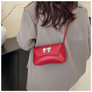 Detail of red crossbody bag featuring woven texture and silver metal bow ornament