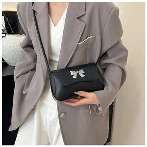 Detail of elegant black crossbody bag with silver bow buckle on model in grey suit