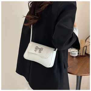 Detail of silver bow clasp and crocodile texture on white faux leather shoulder bag