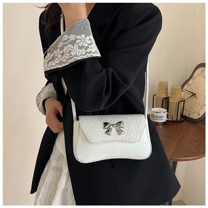 Detail of white faux leather shoulder bag featuring crocodile pattern and silver bow charm