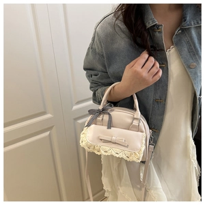 Detail of off-white leather handbag with lace trim, bow, and checkered ribbon on handle