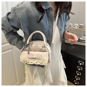 Close-up of cream leather handbag with lace trim, bow, and checkered ribbon on model