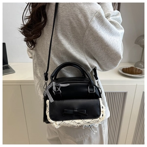 Detail of black crossbody bag with white lace trim and bow on a minimalist desk