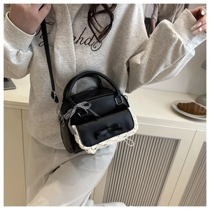 Detail of black pillow bag with white lace trim and bow charm held by a model