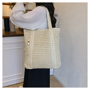 Detail of hollow-out mesh woven tote with wooden beads and tassel charm on shoulder strap