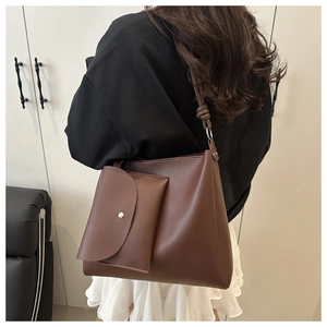 Detail of a brown leather bucket bag with a knotted strap and matching envelope pouch