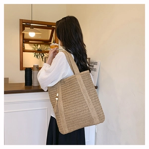 Detail of woven straw tote bag featuring a tassel charm and intricate cross-weave texture