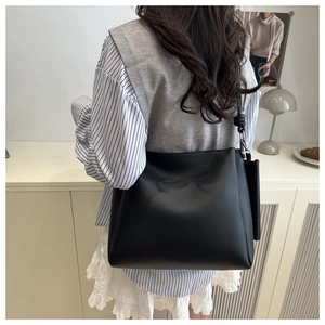 Side view of large black leather tote bag worn by model in a casual indoor setting