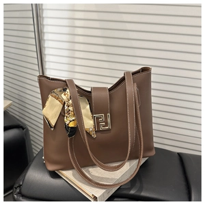 Detail of a brown tote bag with golden geometric clasp and decorative silk scarf accessory