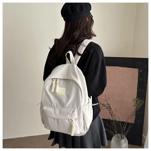 Detail of off-white nylon backpack featuring woven zipper pulls and a yellow smile patch