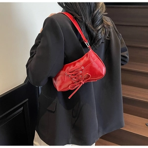 Detail of red glossy leather shoulder bag with cross-straps and bow on black suit