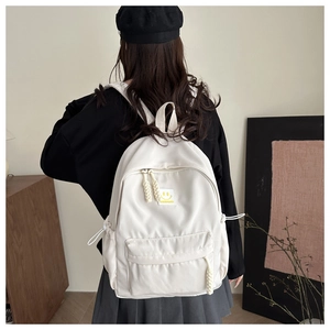 Detail of cream white nylon backpack featuring woven rope zippers and a smiley face patch
