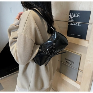 Detail of black glossy shoulder bag featuring stylish side lace-up ribbon decoration