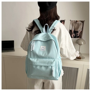Close-up of light blue nylon backpack with front zipper pocket and white smile logo label
