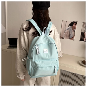 Close-up of light blue canvas backpack featuring a smile patch and woven rope zipper