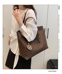 Detail of a large brown tote bag with M-letter pattern and golden logo charm