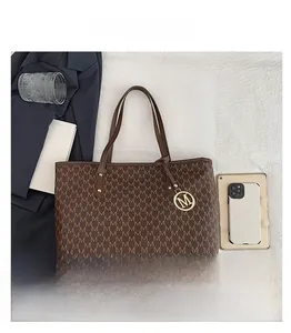 Flat lay detail of a dark brown monogram tote bag with gold M-logo charm on white fabric