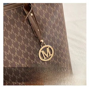 Detail of brown tote bag featuring M monogram pattern and golden metal logo pendant