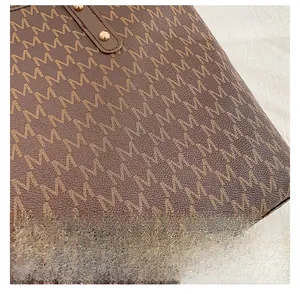 Macro shot of brown leather tote featuring M-letter pattern and gold rivet details