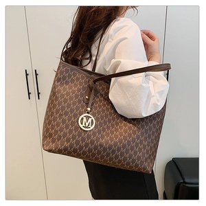 Detail of coffee brown monogram tote bag with golden M charm and long shoulder strap