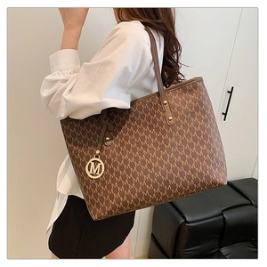 Detail of deep brown tote bag featuring M-letter monogram print and golden charm