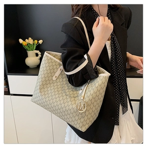 Close-up of beige tote bag featuring letter M pattern and gold metallic logo charm