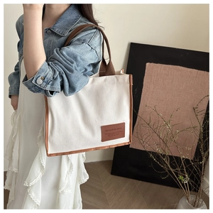 Detail of cream canvas tote bag featuring brown leather trim and Fashion Bag logo patch
