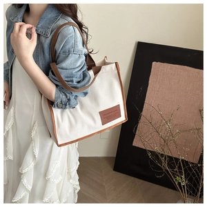 Detail of canvas tote bag showing brown leather reinforced edges and fashion brand tag
