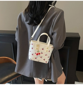 Detail of white bucket bag featuring cherry prints and red cherry charm on a model