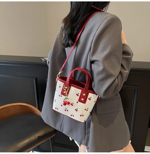 Detail of white leather bucket bag with cherry print and red handles on a model