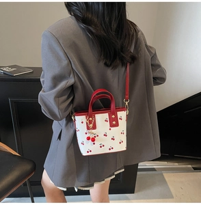 Detail view of model carrying the white cherry print bucket bag with red leather straps