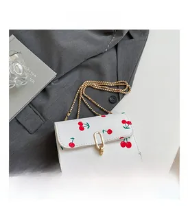 Close-up of white cherry print square crossbody bag with gold chain and metal lock