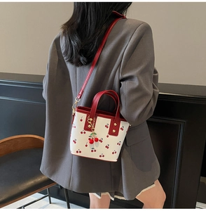 Detail of cherry print bucket bag with red handles and 3D cherry charm accessory