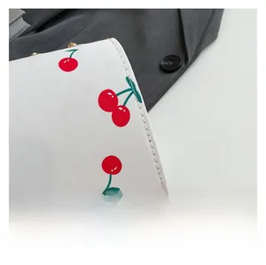 Detailed close-up of cherry pattern printing and stitching on white crossbody bag