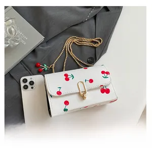Detail of white cherry print crossbody bag with gold chain strap and cherry charms