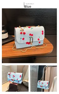 Detail of light blue crossbody bag with cherry prints, gold chain, and cherry charm decoration